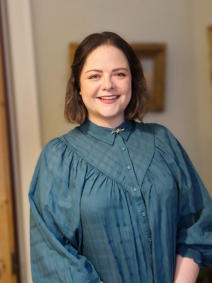 Alexandra, smiling, wearing a teal blouse with a gold bar brooch